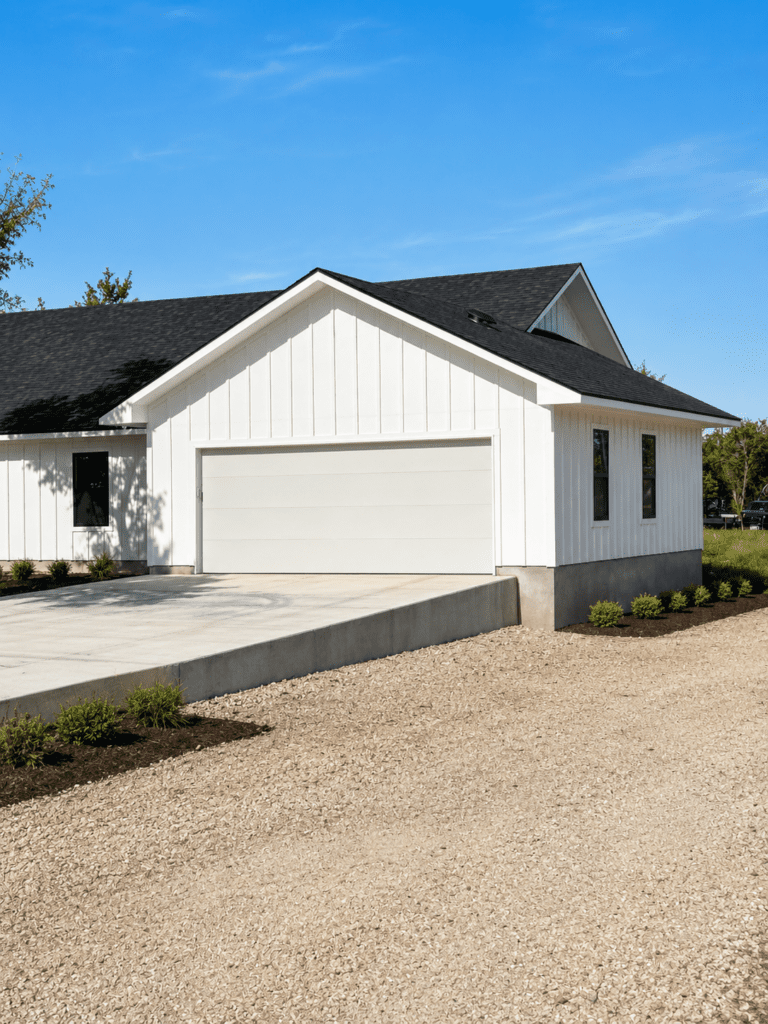 Driftwood custom home build with white board and batten siding, black roof, garage, concrete driveway, and exterior construction