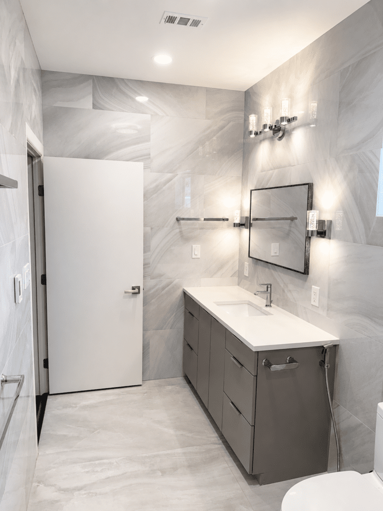 Driftwood Hays County master bathroom remodel with gray tile walls, modern vanity, wall mirror, lighting, tile flooring, and updated bathroom finishes