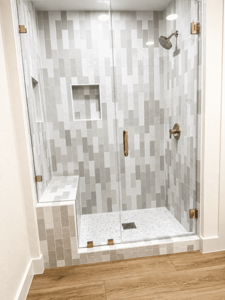Johnson City Blanco County house remodel with glass shower enclosure, gray and white tile walls, shower bench, built-in niche, and updated bathroom finishes